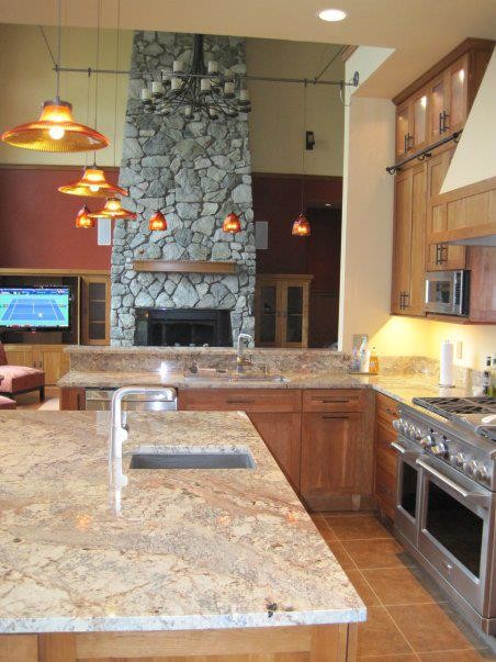 Large mountain style l-shaped porcelain tile and brown floor eat-in kitchen photo with an undermount sink, shaker cabinets, medium tone wood cabinets, granite countertops, orange backsplash, stone slab backsplash, stainless steel appliances and an island