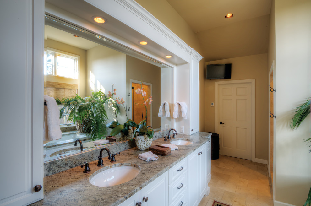 This is an example of a mid-sized traditional master bathroom in Wichita with raised-panel cabinets, white cabinets, beige tile, stone tile, beige walls, an undermount sink, granite benchtops, an undermount tub, an alcove shower, ceramic floors, beige floor and a hinged shower door.