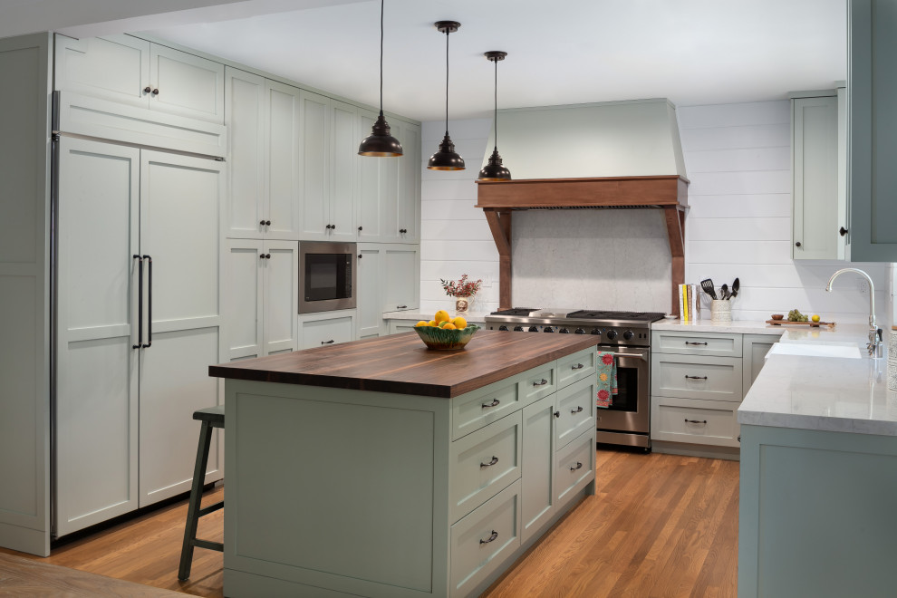 This is an example of a large transitional u-shaped eat-in kitchen in Los Angeles with a farmhouse sink, shaker cabinets, green cabinets, quartz benchtops, white splashback, shiplap splashback, panelled appliances, medium hardwood floors, with island, brown floor and white benchtop.