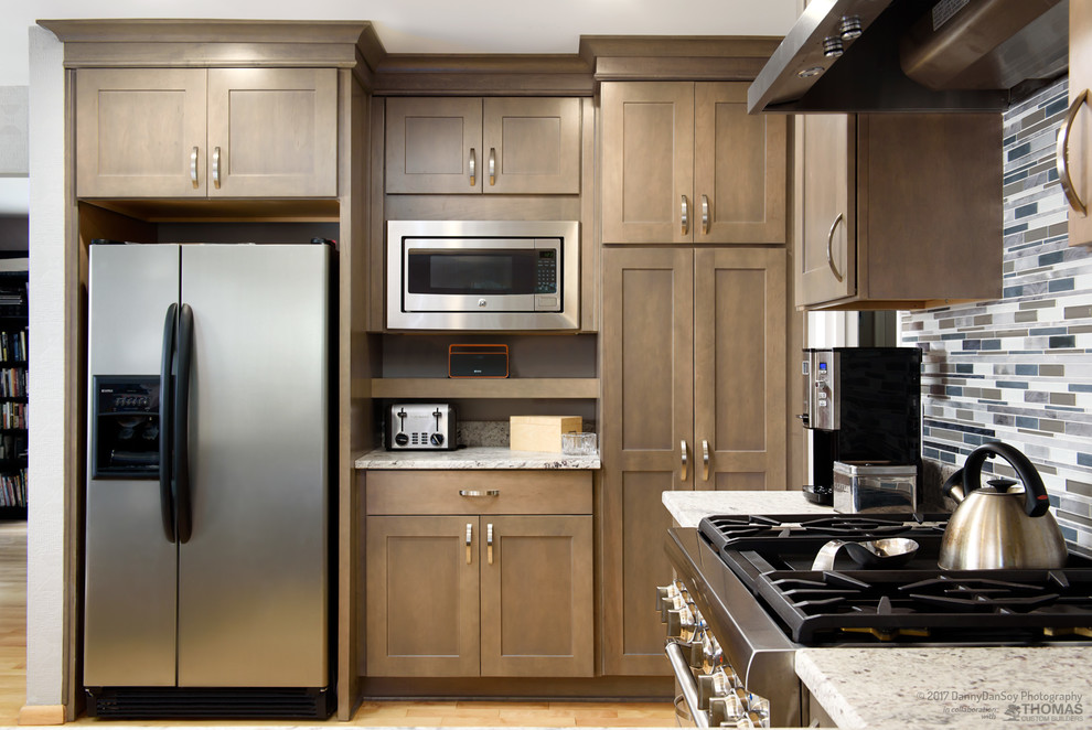 Photo of a mid-sized transitional u-shaped separate kitchen in DC Metro with shaker cabinets, granite benchtops, multi-coloured splashback, stainless steel appliances, light hardwood floors, a double-bowl sink, medium wood cabinets, matchstick tile splashback, a peninsula and brown floor.