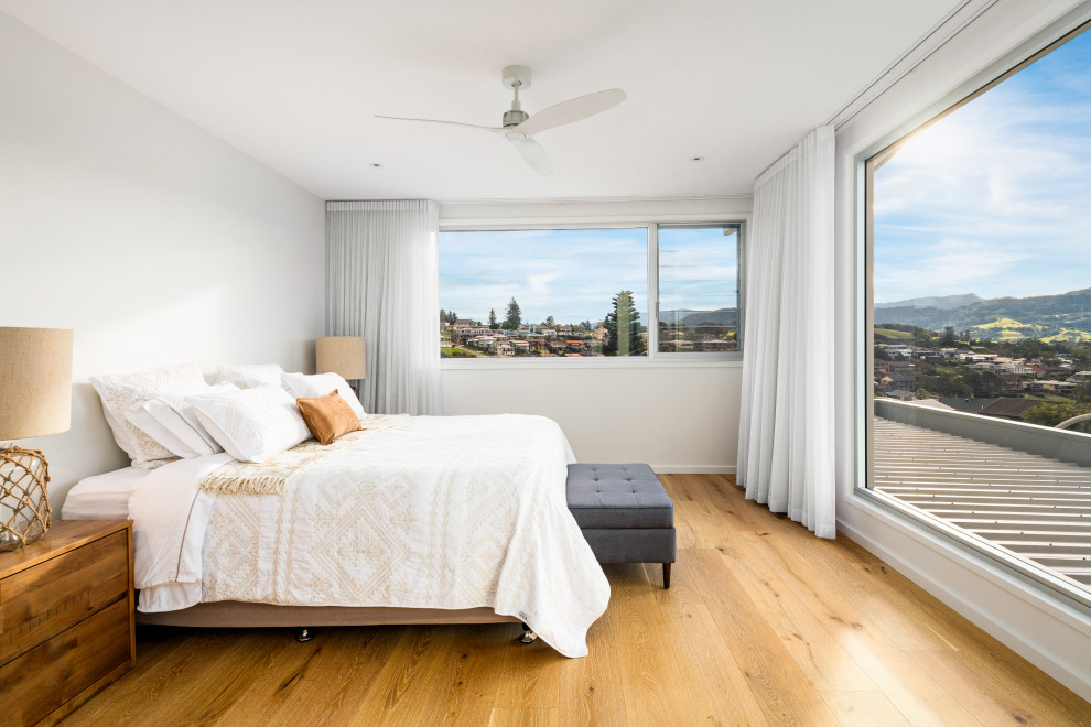 Photo of a large beach style master bedroom in Wollongong with white walls, medium hardwood floors and brown floor.