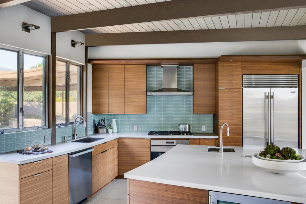 Midcentury l-shaped open plan kitchen in Los Angeles with light wood cabinets, blue splashback, stainless steel appliances, terrazzo floors, with island and white benchtop.