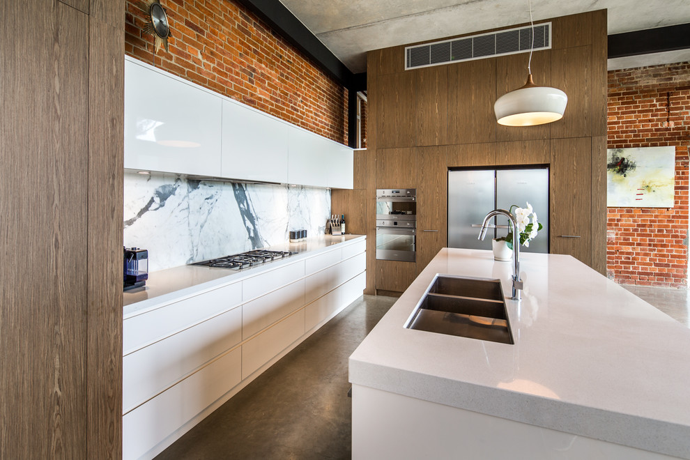 Inspiration for an expansive industrial l-shaped open plan kitchen in Adelaide with an undermount sink, flat-panel cabinets, white cabinets, quartz benchtops, multi-coloured splashback, marble splashback, stainless steel appliances, concrete floors, with island and grey floor.