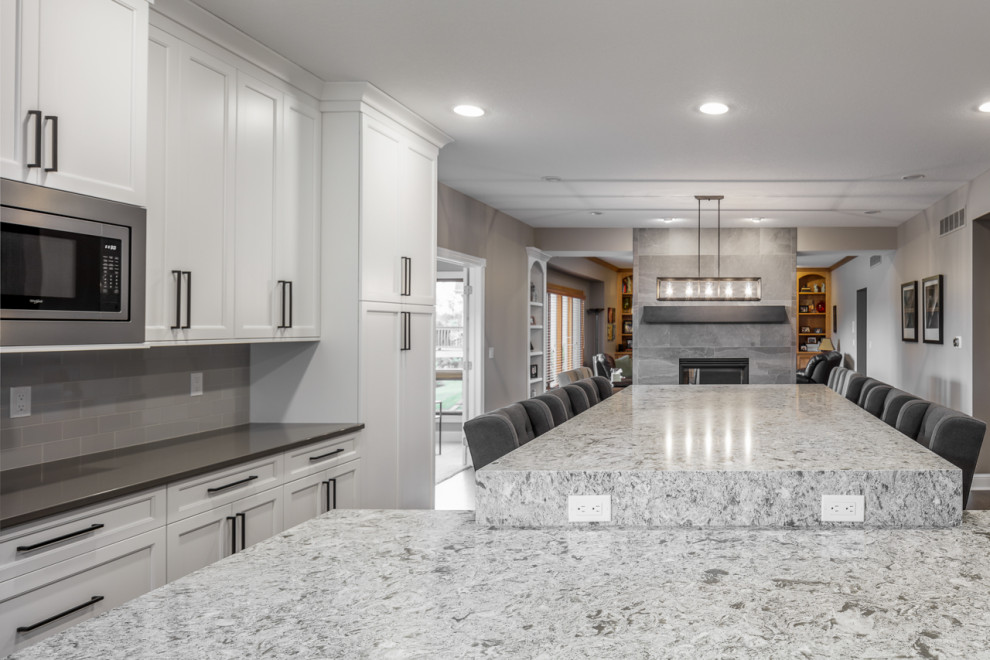 L-shaped brown floor eat-in kitchen photo with shaker cabinets, white cabinets, gray backsplash, stainless steel appliances and an island