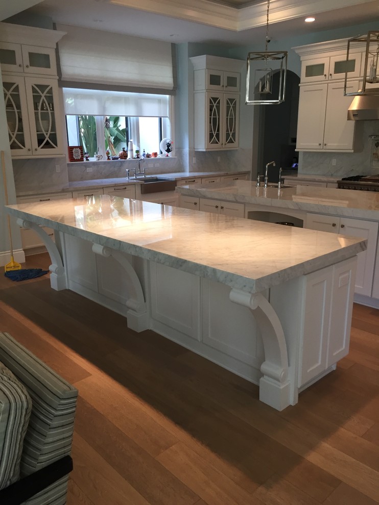 This is an example of a mid-sized modern u-shaped separate kitchen in Miami with a farmhouse sink, shaker cabinets, white cabinets, marble benchtops, white splashback, marble splashback, stainless steel appliances, medium hardwood floors and multiple islands.