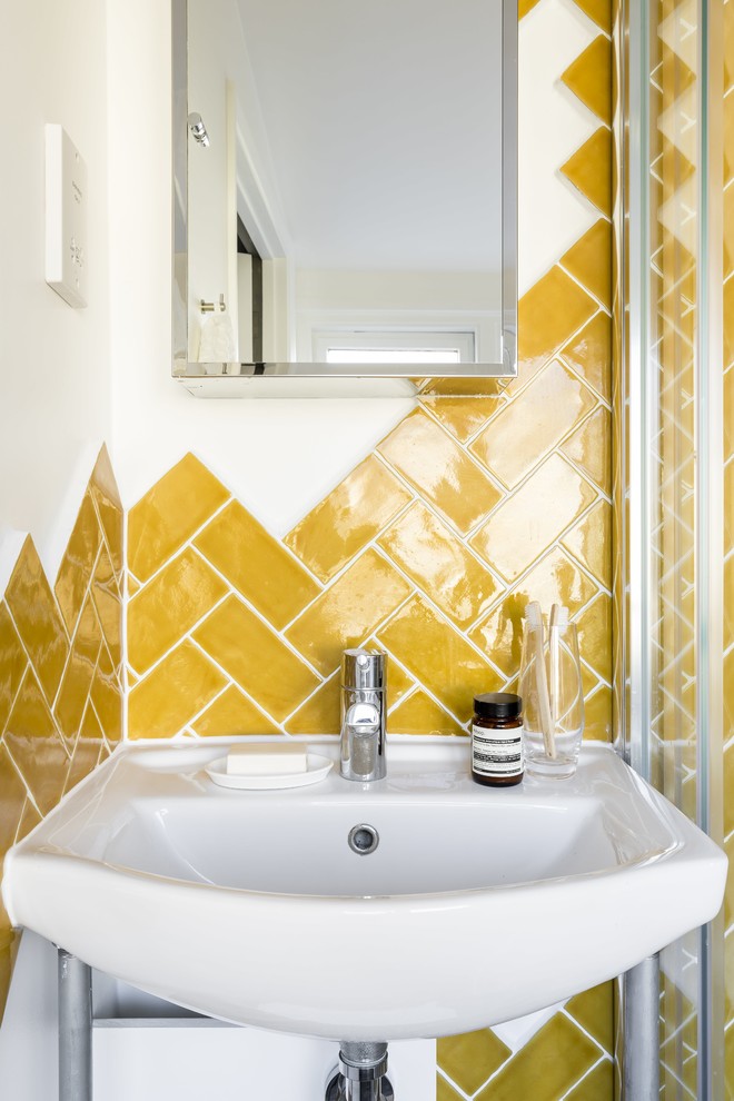 Photo of a small contemporary master bathroom in London with open cabinets, light wood cabinets, a corner shower, a wall-mount toilet, yellow tile, ceramic tile, white walls, concrete floors and a wall-mount sink.