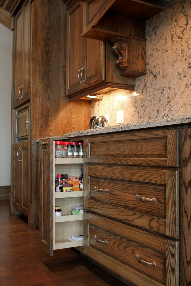 Example of a mid-sized mountain style l-shaped medium tone wood floor open concept kitchen design in Toronto with an undermount sink, raised-panel cabinets, medium tone wood cabinets, granite countertops, multicolored backsplash, stone slab backsplash, stainless steel appliances and an island
