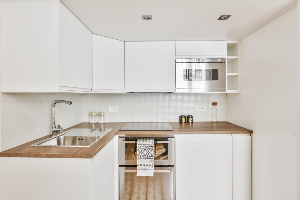 Inspiration for a small contemporary l-shaped open plan kitchen in Paris with a single-bowl sink, white cabinets, wood benchtops, white splashback, stainless steel appliances, medium hardwood floors, no island, brown floor and mosaic tile splashback.