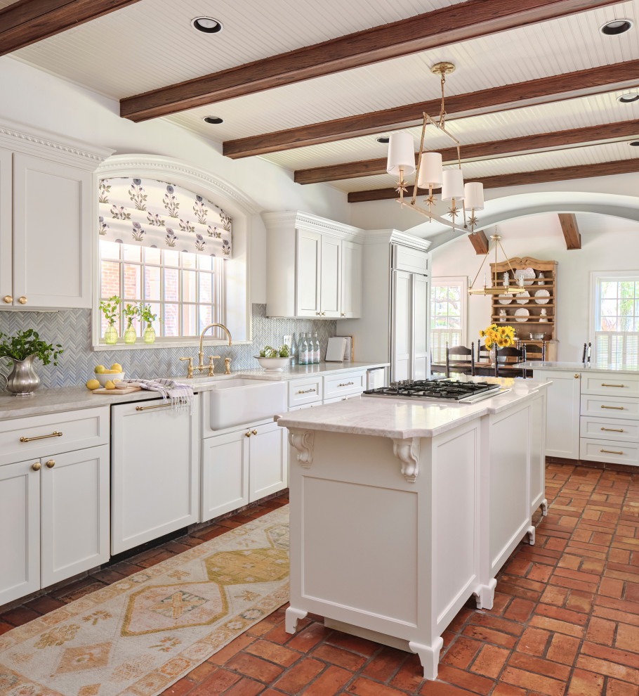 Design ideas for a traditional l-shaped eat-in kitchen in Austin with a farmhouse sink, recessed-panel cabinets, white cabinets, marble benchtops, blue splashback, glass tile splashback, panelled appliances, terra-cotta floors, with island, white benchtop and exposed beam.