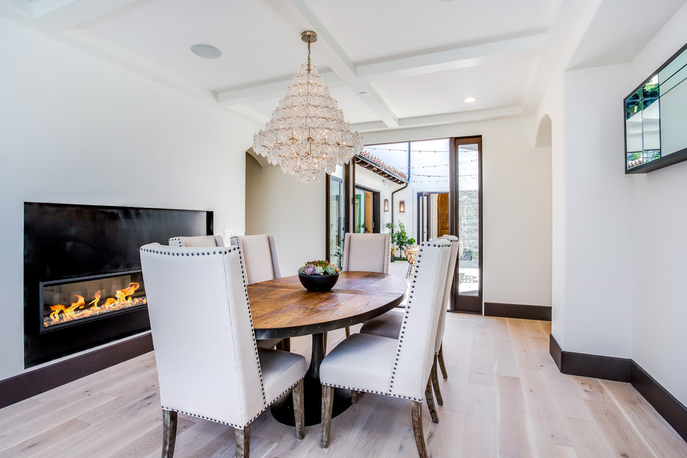 Inspiration for a mediterranean separate dining room in Orange County with white walls, light hardwood floors, a ribbon fireplace, beige floor and a metal fireplace surround.