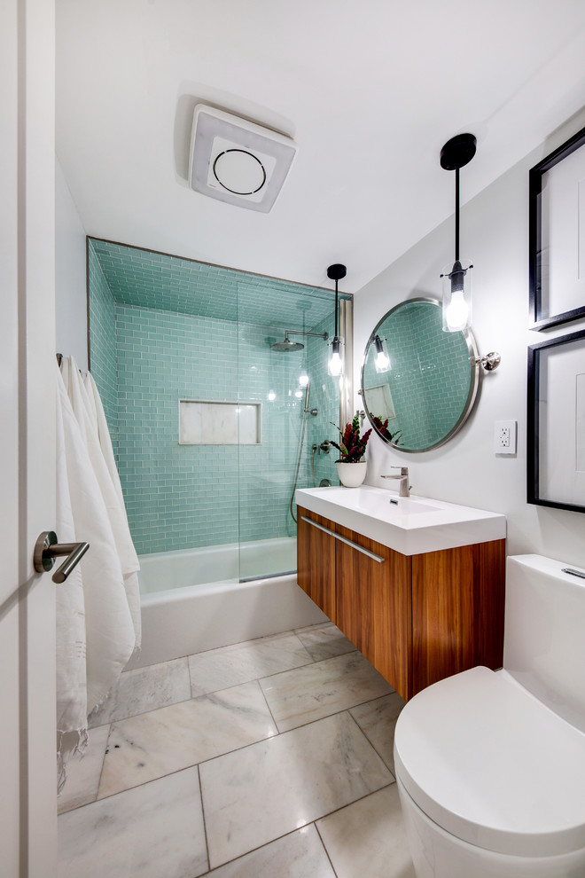 This is an example of a small modern master bathroom in New York with flat-panel cabinets, medium wood cabinets, an alcove tub, a shower/bathtub combo, a one-piece toilet, green tile, subway tile, grey walls, marble floors, a wall-mount sink, engineered quartz benchtops, white floor, an open shower and white benchtops.