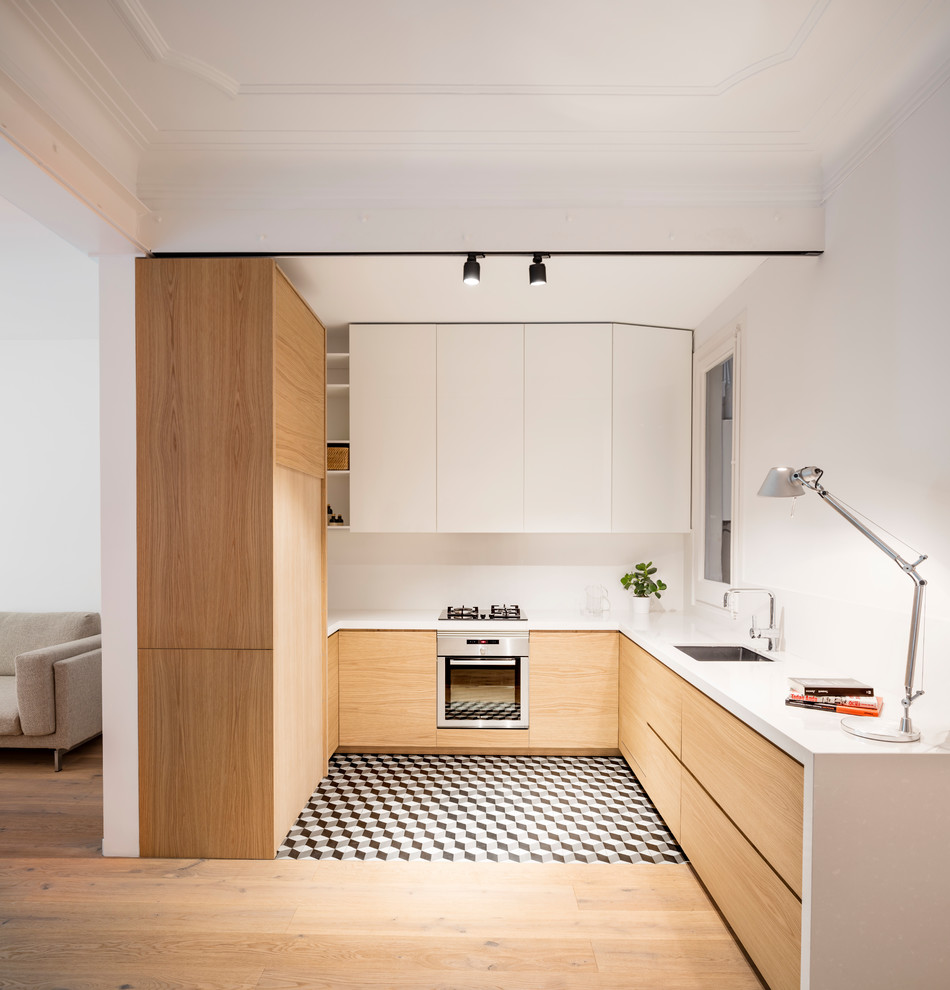 Photo of a mid-sized scandinavian u-shaped open plan kitchen in Barcelona with flat-panel cabinets, white splashback, stainless steel appliances, ceramic floors, no island, multi-coloured floor, a single-bowl sink, light wood cabinets and quartz benchtops.