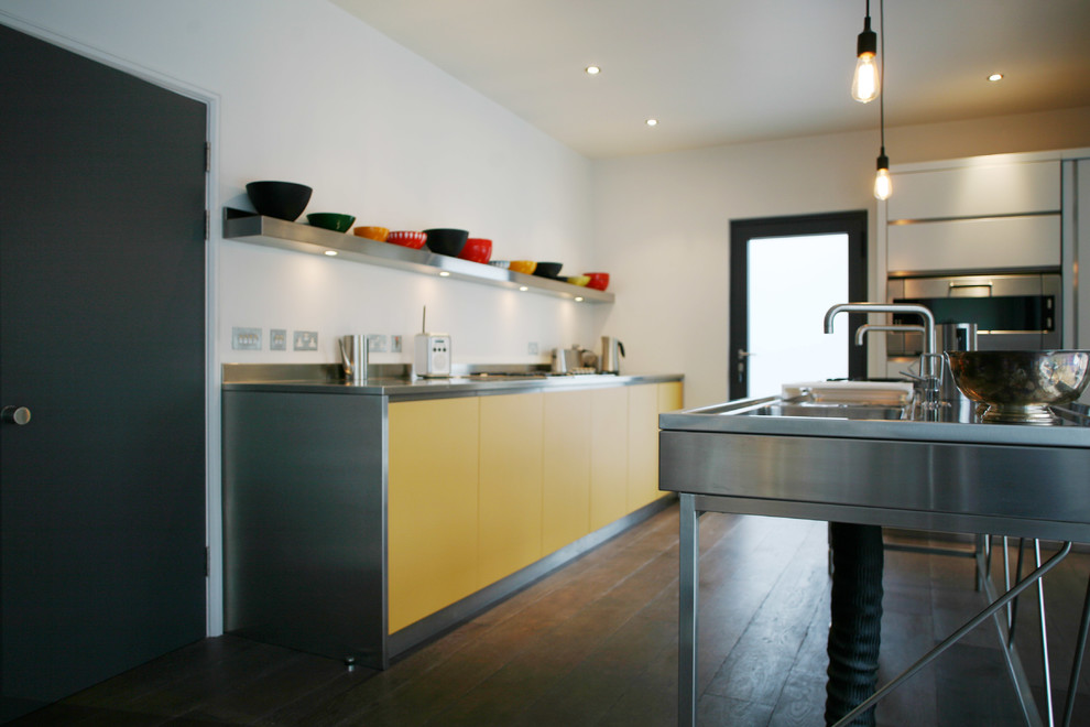 This is an example of a mid-sized contemporary l-shaped eat-in kitchen in London with a double-bowl sink, flat-panel cabinets, yellow cabinets, stainless steel benchtops, white splashback, stainless steel appliances, dark hardwood floors and with island.