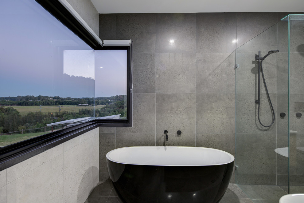 This is an example of an industrial bathroom in Sunshine Coast with a freestanding tub, a double shower, porcelain tile, porcelain floors, grey floor, a hinged shower door, gray tile, grey walls, glass benchtops and white benchtops.