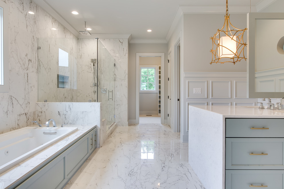 Photo of an expansive transitional master bathroom in Nashville with shaker cabinets, a drop-in tub, a corner shower, white walls, white floor, a hinged shower door, blue cabinets, gray tile, marble, marble floors, marble benchtops and white benchtops.