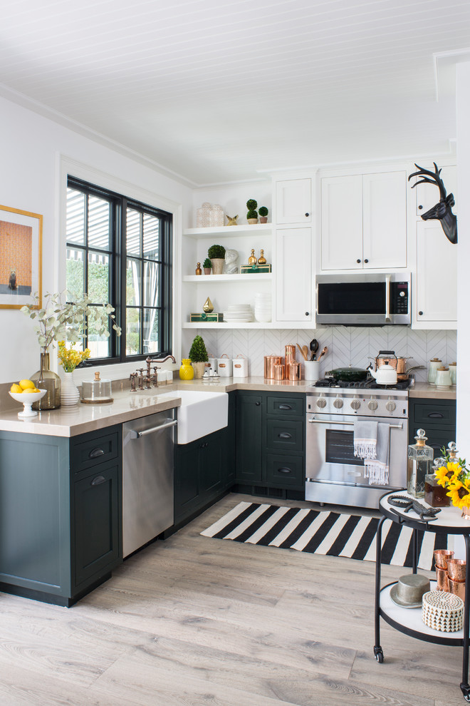 Photo of a mid-sized transitional l-shaped kitchen in Los Angeles with a farmhouse sink, shaker cabinets, green cabinets, white splashback, stainless steel appliances, light hardwood floors, no island, beige floor and porcelain splashback.