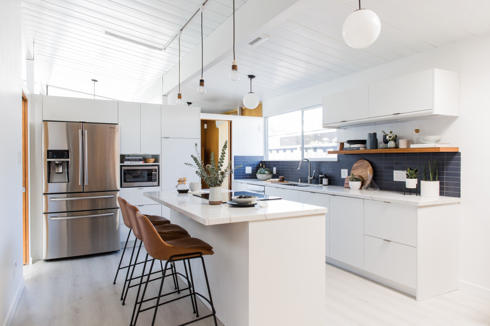 Mid-sized midcentury l-shaped kitchen in San Francisco with an undermount sink, flat-panel cabinets, white cabinets, quartz benchtops, blue splashback, ceramic splashback, stainless steel appliances, vinyl floors, with island, white benchtop, exposed beam, timber, vaulted and white floor.