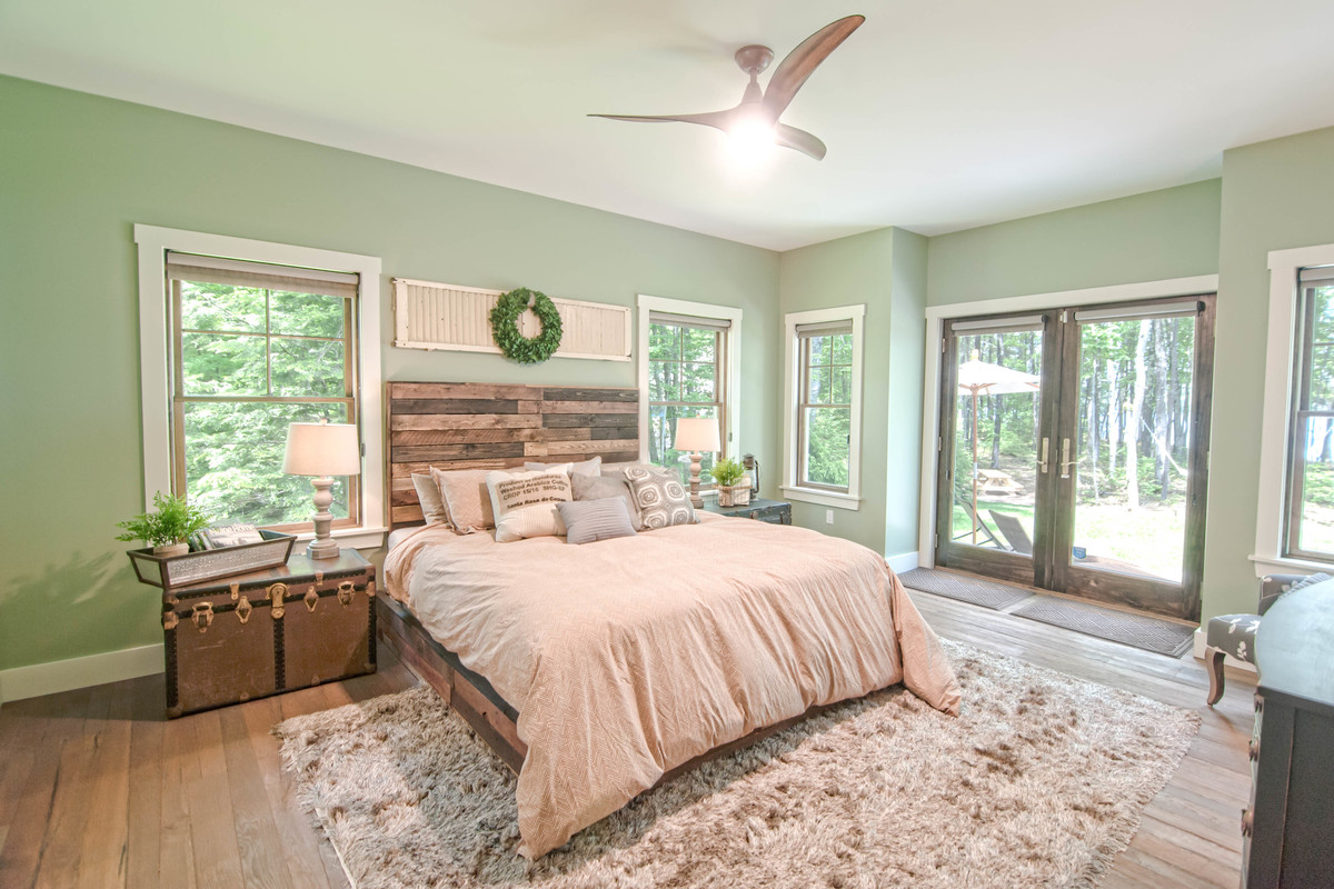 This is an example of a large arts and crafts master bedroom in Portland Maine with green walls, medium hardwood floors and brown floor.