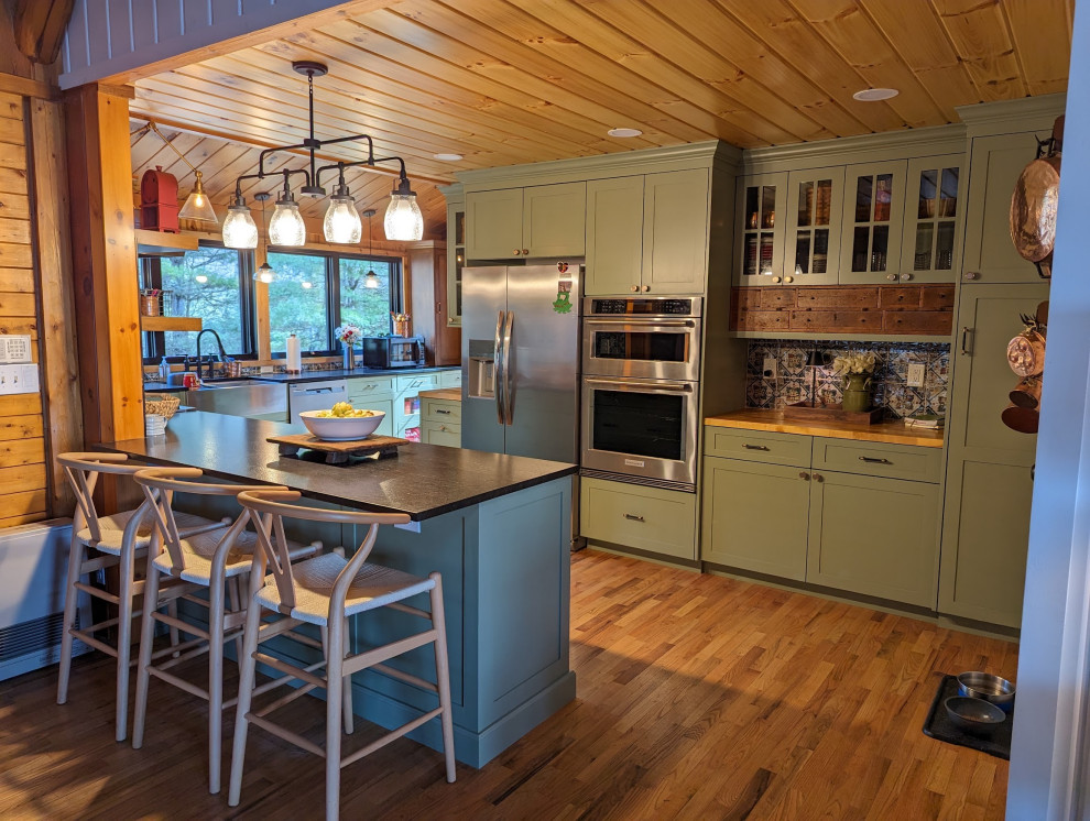 Mid-sized mountain style l-shaped medium tone wood floor, brown floor and wood ceiling eat-in kitchen photo with a farmhouse sink, shaker cabinets, green cabinets, granite countertops, multicolored backsplash, ceramic backsplash, stainless steel appliances and black countertops
