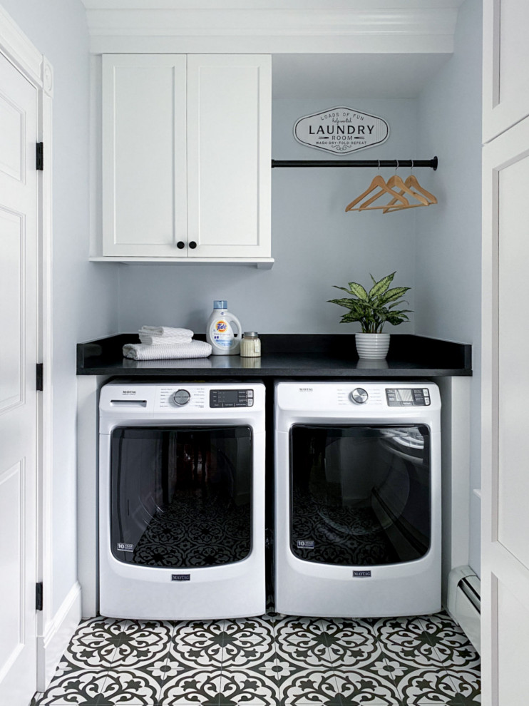 Foto di una sala lavanderia tradizionale con ante in stile shaker, ante bianche, top in granito, pareti blu, pavimento in gres porcellanato, lavatrice e asciugatrice affiancate, pavimento nero e top nero
