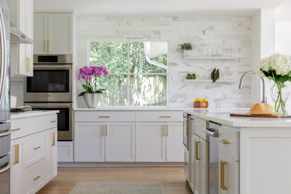 Inspiration for a midcentury l-shaped open plan kitchen in Austin with an undermount sink, shaker cabinets, grey cabinets, marble splashback, stainless steel appliances, light hardwood floors, with island and white benchtop.