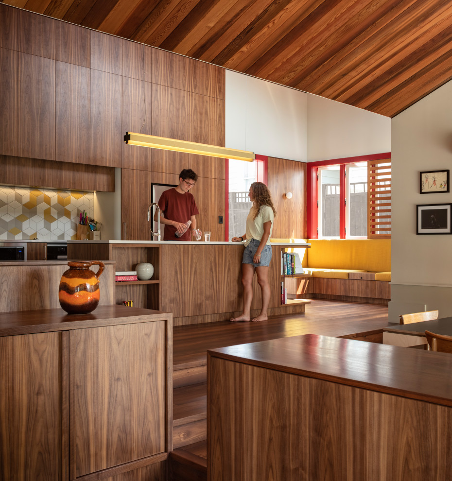 Photo of a midcentury open plan kitchen in Auckland with flat-panel cabinets, dark wood cabinets, multi-coloured splashback, dark hardwood floors, with island, brown floor, vaulted and wood.