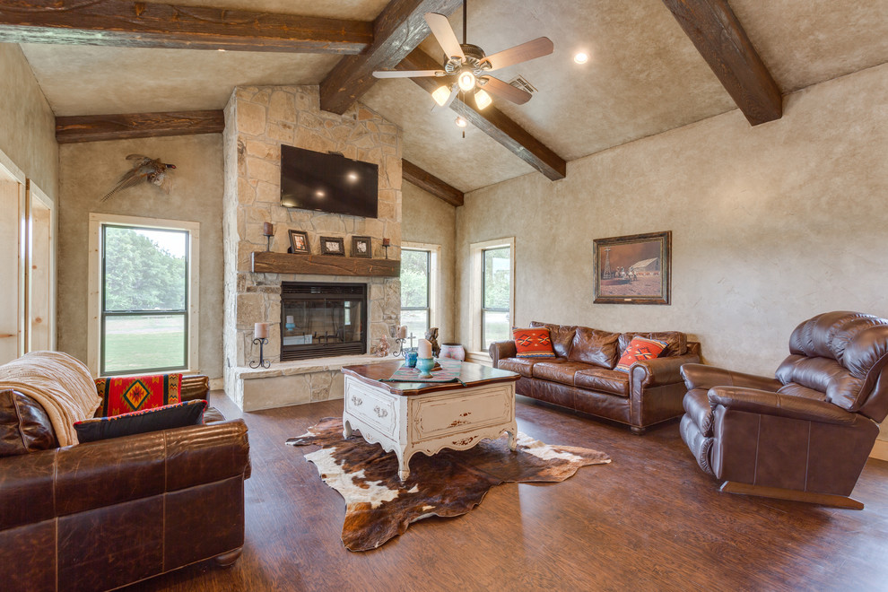 Inspiration for a mid-sized country open concept living room in Dallas with beige walls, vinyl floors, a standard fireplace, a stone fireplace surround, a wall-mounted tv and brown floor.