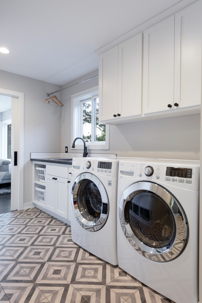 Design ideas for a mid-sized midcentury single-wall dedicated laundry room in Minneapolis with a drop-in sink, shaker cabinets, white cabinets, quartzite benchtops, grey walls, porcelain floors, a side-by-side washer and dryer and grey benchtop.