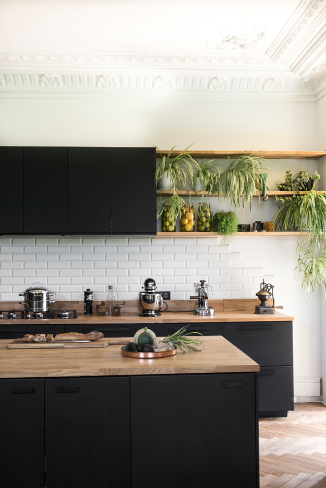 Design ideas for a large eclectic galley kitchen in Other with black cabinets, wood benchtops, white splashback, subway tile splashback, with island, brown floor, brown benchtop, flat-panel cabinets and medium hardwood floors.