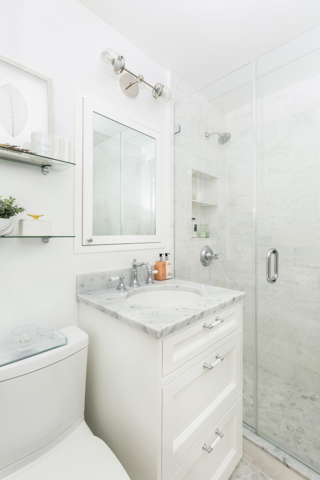 This is an example of a small coastal ensuite bathroom in New York with recessed-panel cabinets, white cabinets, all types of shower, a one-piece toilet, white tiles, marble tiles, white walls, marble flooring, a submerged sink, marble worktops, white floors, a hinged door, white worktops, a single sink and a freestanding vanity unit.