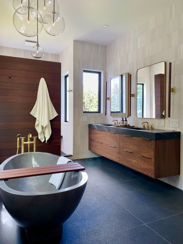 Photo of a large contemporary bathroom in New York with flat-panel cabinets, brown cabinets, a freestanding tub, an alcove shower, a bidet, beige tile, ceramic tile, white walls, porcelain floors, an undermount sink, soapstone benchtops, black floor, an open shower, black benchtops, a shower seat, a double vanity, a floating vanity, vaulted and wood walls.