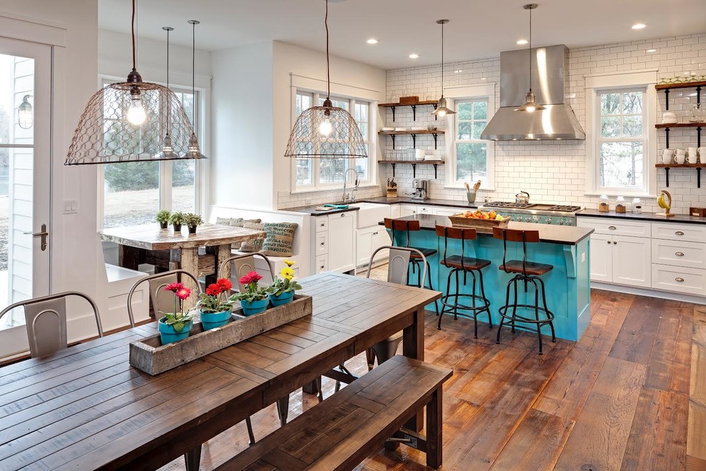 Inspiration for a country l-shaped eat-in kitchen in Chicago with a farmhouse sink, shaker cabinets, white cabinets, white splashback, subway tile splashback, stainless steel appliances, medium hardwood floors and with island.