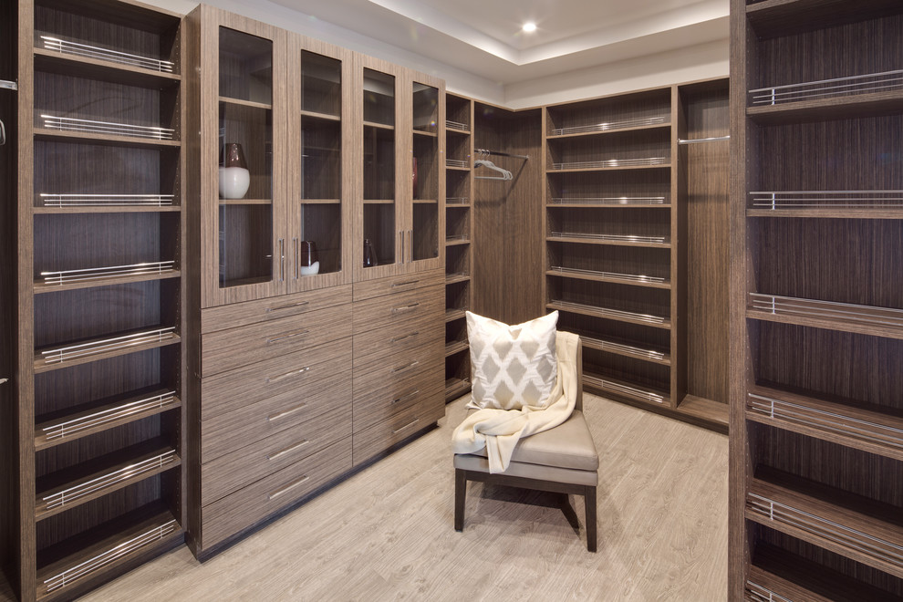 Example of a large trendy gender-neutral walk-in closet design in Los Angeles with glass-front cabinets and dark wood cabinets