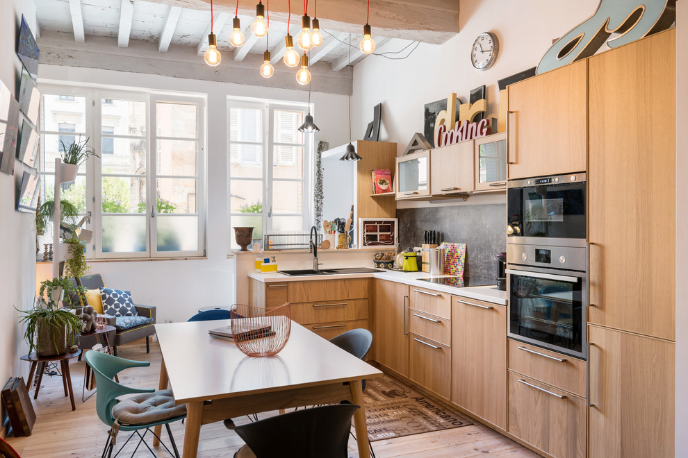 This is an example of an eclectic l-shaped eat-in kitchen in Lyon with a drop-in sink, flat-panel cabinets, medium wood cabinets, black splashback, black appliances, light hardwood floors, no island and beige floor.
