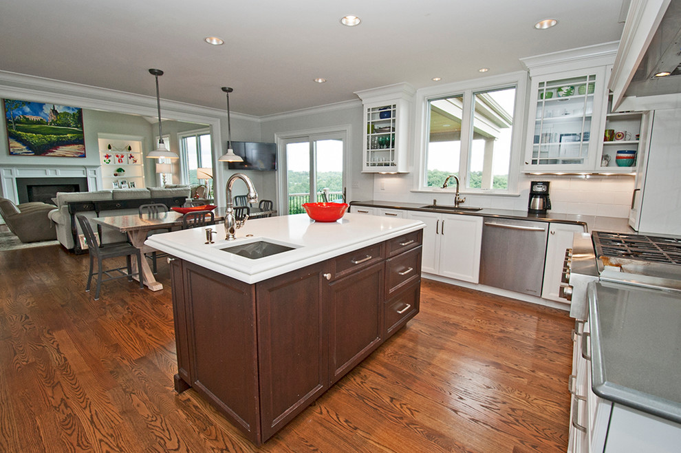 Mid-sized transitional l-shaped medium tone wood floor and brown floor open concept kitchen photo with an undermount sink, glass-front cabinets, white cabinets, white backsplash, subway tile backsplash, stainless steel appliances, an island and quartz countertops