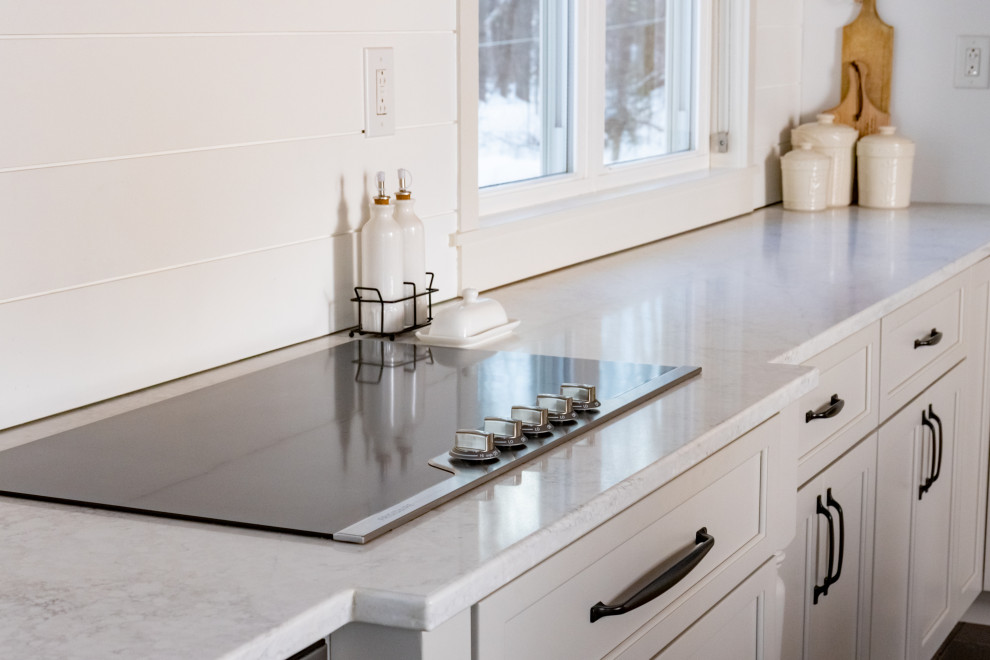 This is an example of a large country l-shaped eat-in kitchen in Portland Maine with a farmhouse sink, shaker cabinets, grey cabinets, marble benchtops, white splashback, shiplap splashback, stainless steel appliances, dark hardwood floors, with island, brown floor, white benchtop and exposed beam.