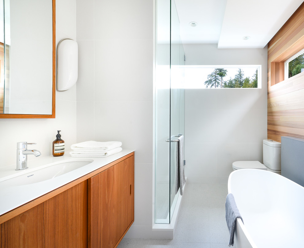 Design ideas for a mid-sized midcentury master bathroom in Vancouver with flat-panel cabinets, medium wood cabinets, engineered quartz benchtops, a freestanding tub, a two-piece toilet, white tile, porcelain tile, white walls, porcelain floors, an undermount sink and an alcove shower.
