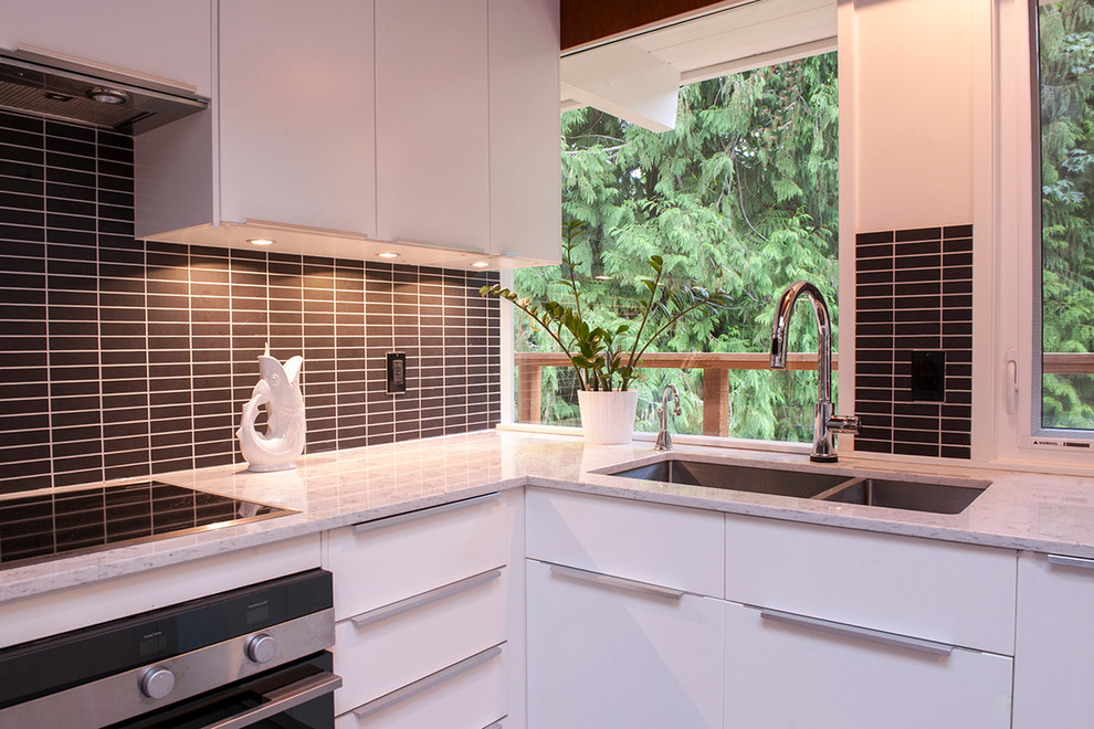 This is an example of a mid-sized midcentury u-shaped eat-in kitchen in Vancouver with a drop-in sink, flat-panel cabinets, white cabinets, quartz benchtops, black splashback, subway tile splashback, stainless steel appliances and ceramic floors.