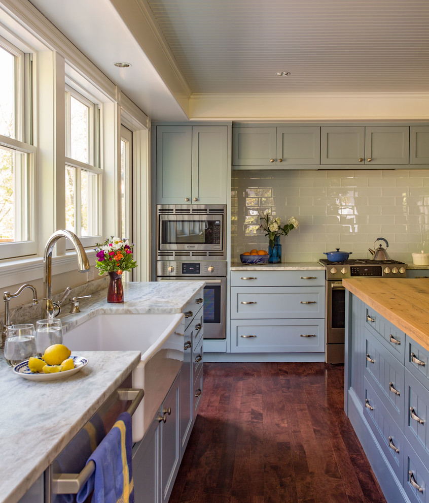 Photo of a mid-sized country l-shaped kitchen in Boston with a farmhouse sink, shaker cabinets, blue cabinets, granite benchtops, stainless steel appliances, dark hardwood floors and white splashback.