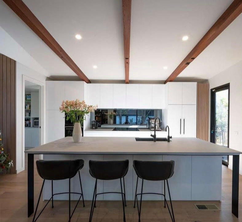Photo of a mid-sized contemporary galley open plan kitchen with an undermount sink, flat-panel cabinets, white cabinets, quartz benchtops, black splashback, glass tile splashback, panelled appliances, medium hardwood floors, with island, brown floor, grey benchtop and vaulted.