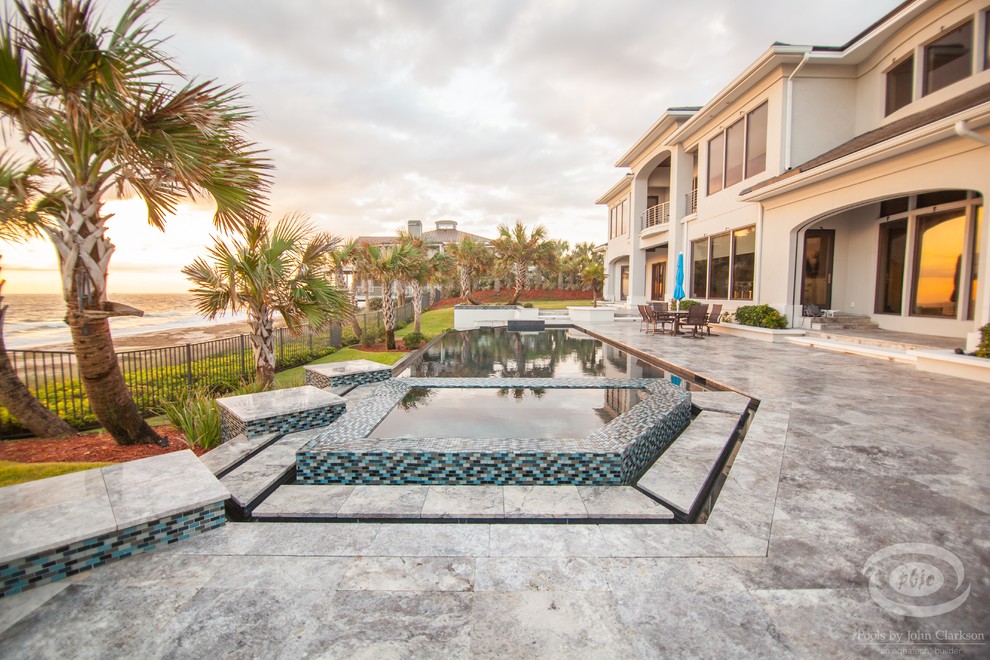 Inspiration for a large contemporary backyard custom-shaped infinity pool in Jacksonville with natural stone pavers.
