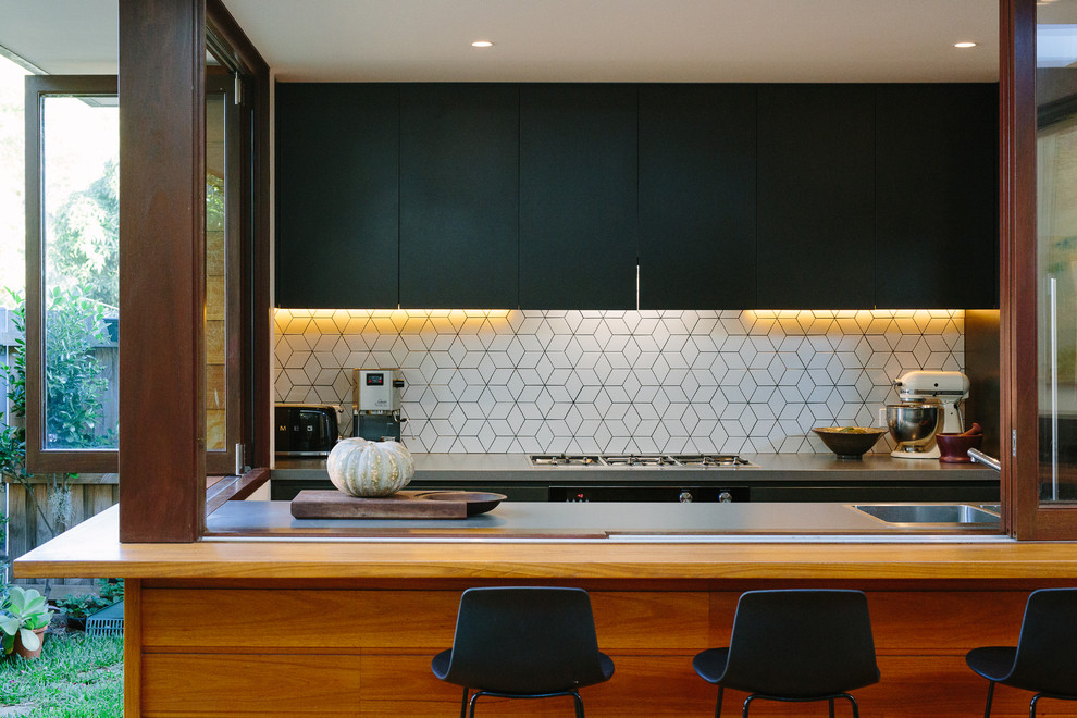 Mid-sized contemporary u-shaped open plan kitchen in Sydney with an integrated sink, flat-panel cabinets, black cabinets, concrete benchtops, white splashback, medium hardwood floors and no island.