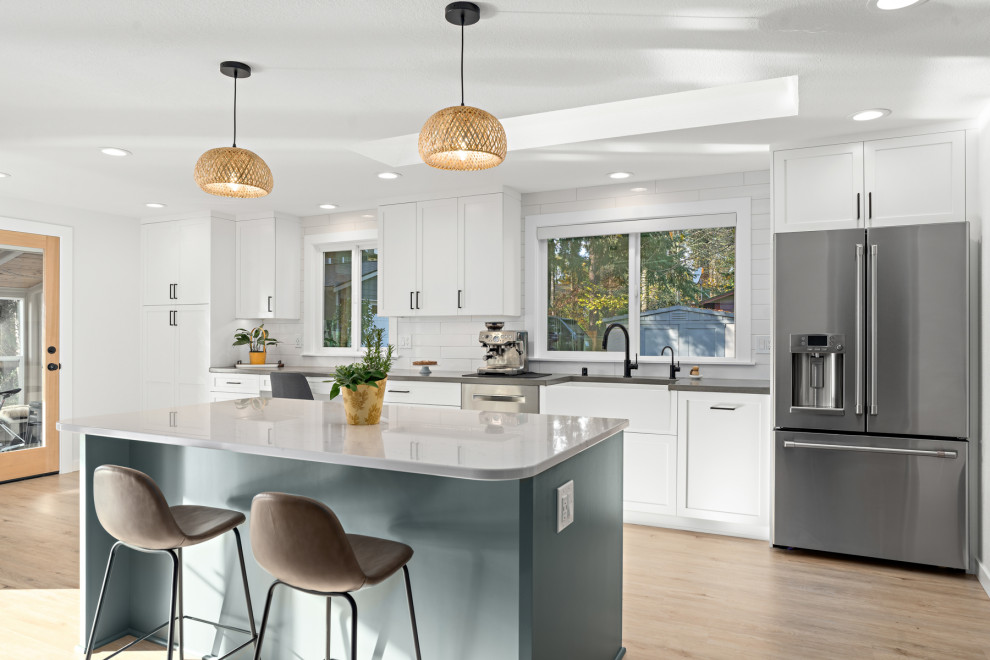 Design ideas for a large arts and crafts galley open plan kitchen in Seattle with a farmhouse sink, recessed-panel cabinets, white cabinets, quartz benchtops, white splashback, subway tile splashback, stainless steel appliances, light hardwood floors, with island, beige floor and white benchtop.