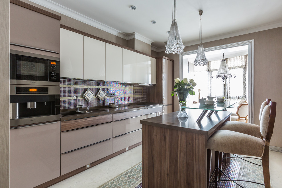 Transitional galley separate kitchen in Other with solid surface benchtops, travertine floors, with island, flat-panel cabinets, beige cabinets, mosaic tile splashback, multi-coloured floor, a drop-in sink and stainless steel appliances.