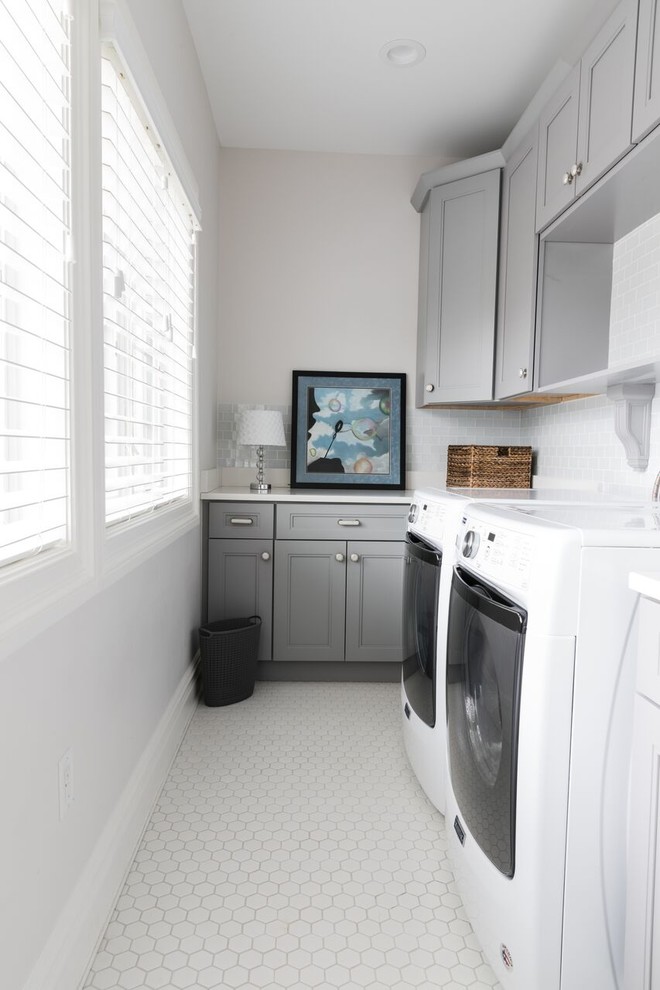 Photo of a small traditional single-wall dedicated laundry room in New York with an undermount sink, recessed-panel cabinets, grey cabinets, solid surface benchtops, grey walls, porcelain floors, a side-by-side washer and dryer, white floor and white benchtop.