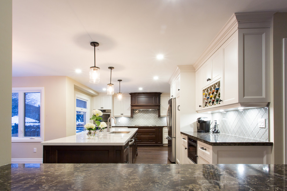 Large transitional l-shaped dark wood floor eat-in kitchen photo in Orange County with a double-bowl sink, recessed-panel cabinets, white cabinets, granite countertops, gray backsplash, glass tile backsplash, stainless steel appliances and an island