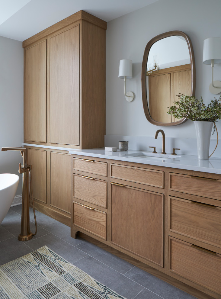 Photo of a large classic ensuite bathroom in Chicago with beaded cabinets, brown cabinets, a freestanding bath, a walk-in shower, white tiles, white walls, ceramic flooring, a built-in sink, quartz worktops, grey floors, a sliding door, white worktops, a wall niche, double sinks and a built in vanity unit.