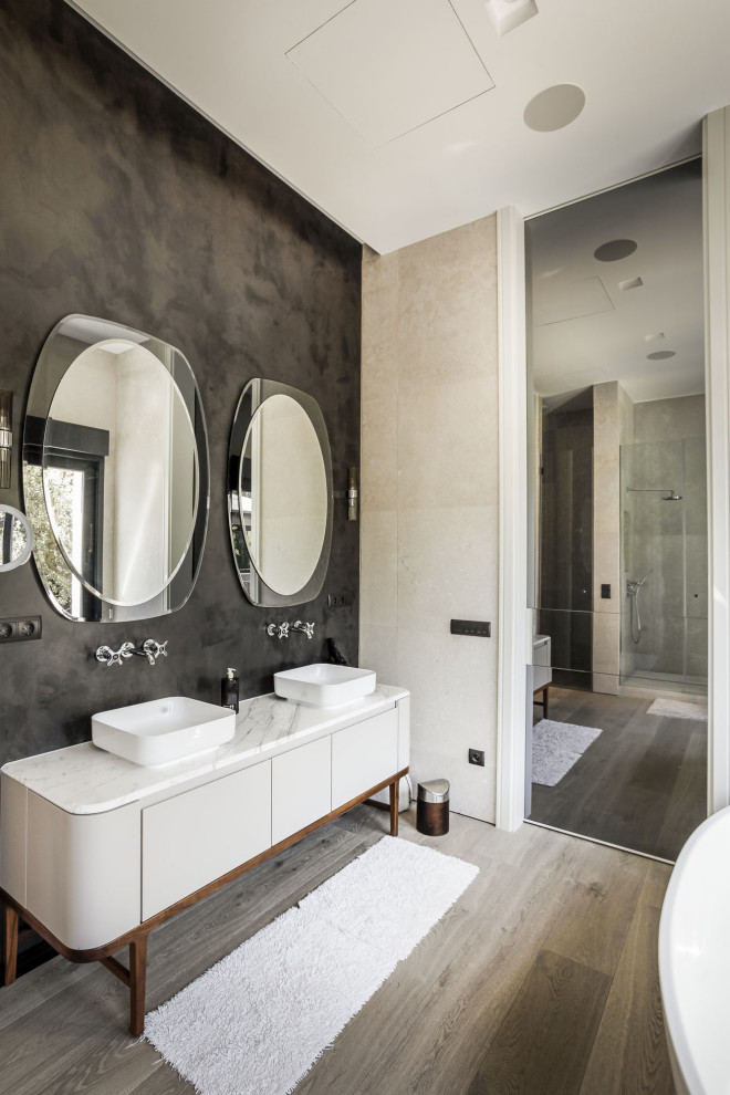 This is an example of a contemporary master bathroom in Madrid with flat-panel cabinets, grey cabinets, black walls, light hardwood floors, a vessel sink, white benchtops, a double vanity and a freestanding vanity.