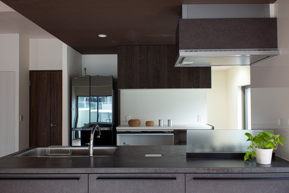 Bild på ett mellanstort rustikt grå linjärt grått kök med öppen planlösning, med en undermonterad diskho, luckor med profilerade fronter, skåp i slitet trä, bänkskiva i rostfritt stål, vitt stänkskydd, svarta vitvaror, mellanmörkt trägolv, en halv köksö och brunt golv