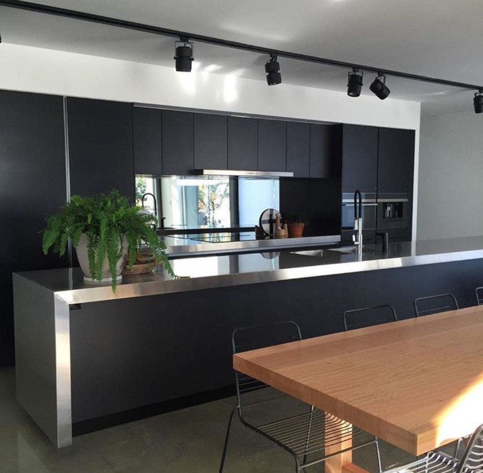 Design ideas for a large contemporary galley eat-in kitchen in Sydney with an integrated sink, black cabinets, stainless steel benchtops, mirror splashback, panelled appliances, concrete floors, with island and grey floor.